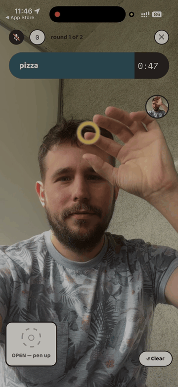 Inkfish gameplay: a player gets the word pizza, pinches their thumb and index finger to draw a pizza in the air in front of the camera, and the drawing appears on the live video